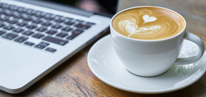 Tasse de café, arrosé de lait en crème et forme de coeur à côté d'un ordinateur portable'